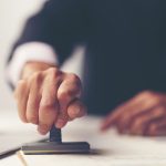 close up of a person's hand stamping with approved stamp on document at desk